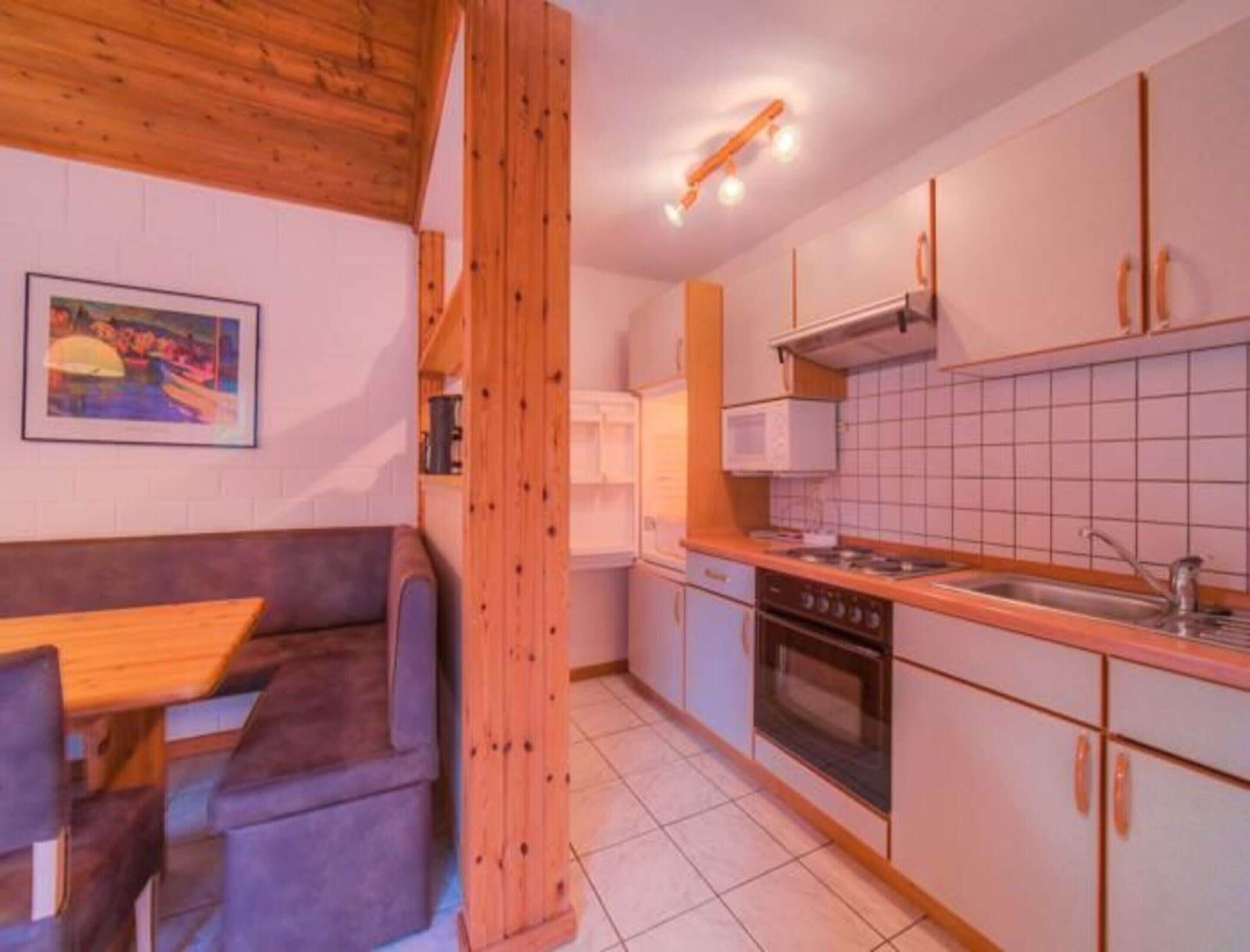 Een compacte keuken met een houten plafond, een zithoek met een tafel en een bank, en een betegelde spatwand.