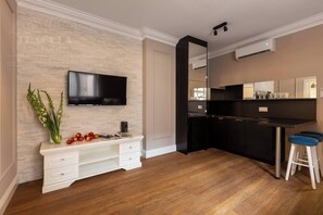 A modern kitchen with a flat-screen TV, wooden flooring, and a white console table with decorative items.