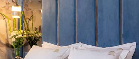 A bed with white linens and a blue headboard, a hanging light fixture, and a vase with flowers.