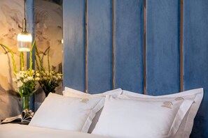 Un lit avec du linge de lit blanc et une tête de lit bleue, un luminaire suspendu et un vase rempli de fleurs.