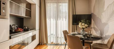 A modern kitchen with built-in appliances, a dining area with a round table and chairs, and a large window with sheer curtains.