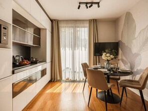 Une cuisine moderne dotée d’appareils électroménagers intégrés, un coin repas avec une table ronde et des chaises, et une grande fenêtre agrémentée de rideaux légers.