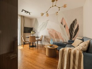 A modern living room with a sofa, coffee table, and a dining area with chairs and a TV.