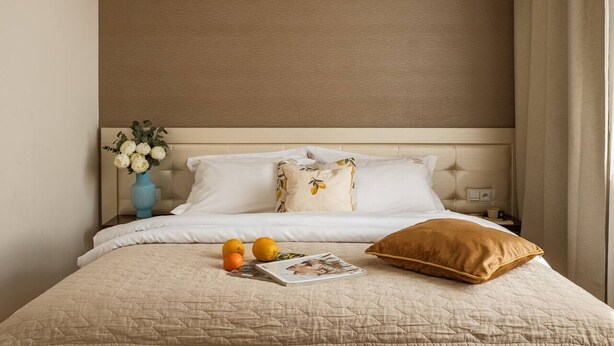 Una habitación de hotel con cama, mesita de noche, un jarrón con flores y ventana con cortinas.