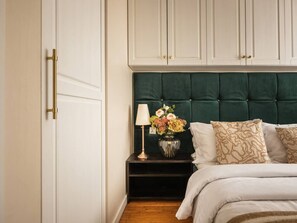 Ein Schlafzimmer mit einem Bett, einem Nachttisch mit Lampe, einer Blumenvase und einem Kleiderschrank.