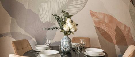 Une table à manger ornée d’un vase de fleurs, de assiettes blanches et de verres.