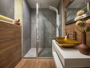 A modern bathroom with a glass-enclosed shower, a gold vessel sink, and a wooden vanity.