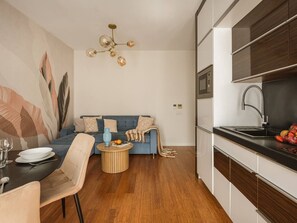 A modern kitchen with a built-in oven, a dining area with a round table and chairs, and a living area with a sofa and a decorative wall.
