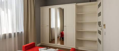 A hotel room with a bed, red chairs, a wardrobe, and a mirror.
