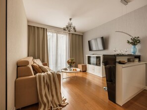 Una sala de estar moderna con un sofá, una mesa de centro, un televisor y una zona de cocina con un refrigerador.