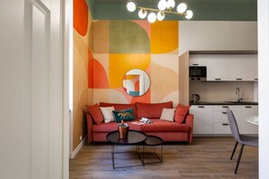 A compact living space with a sofa, a coffee table, a dining area, and a kitchen with cabinets and a microwave. - Apartment Pistacchio with balcony (Kraków – Old Town)