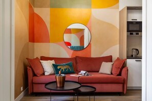 A modern living room with a red sofa, a coffee table, and a kitchen area with a kettle.
