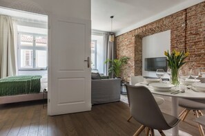 Ein modernes Wohnzimmer mit Essbereich, einer Ziegelwand, einem großen Fenster und einem Flachbildfernseher.