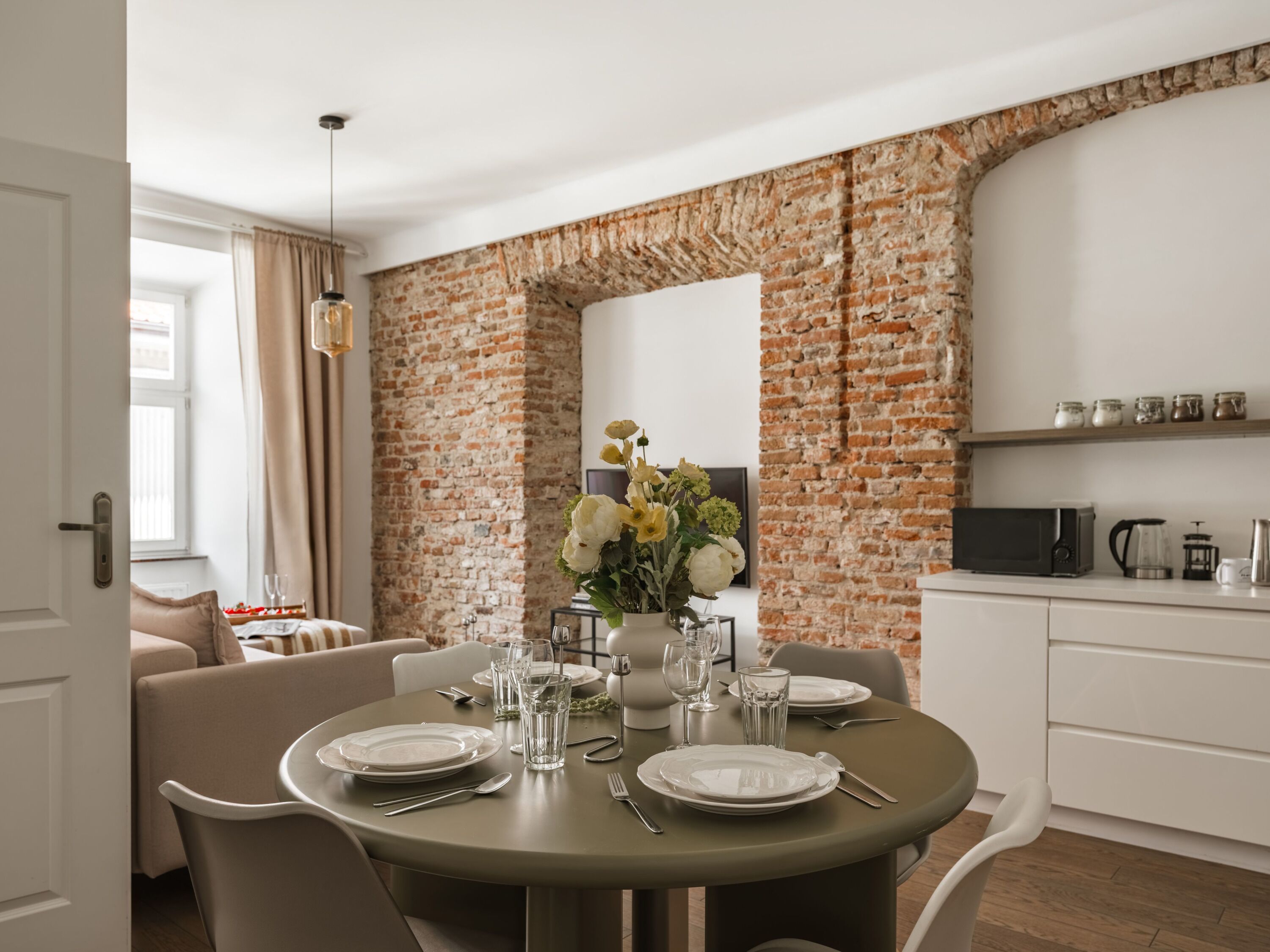 A dining area with a brick wall, a round table set for four, and a kitchen area with a microwave and coffee maker.