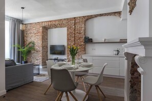 Un espacio habitable moderno con una pared de ladrillo decorativa, una zona de comedor con mobiliario blanco y un televisor de pantalla plana sobre la chimenea.