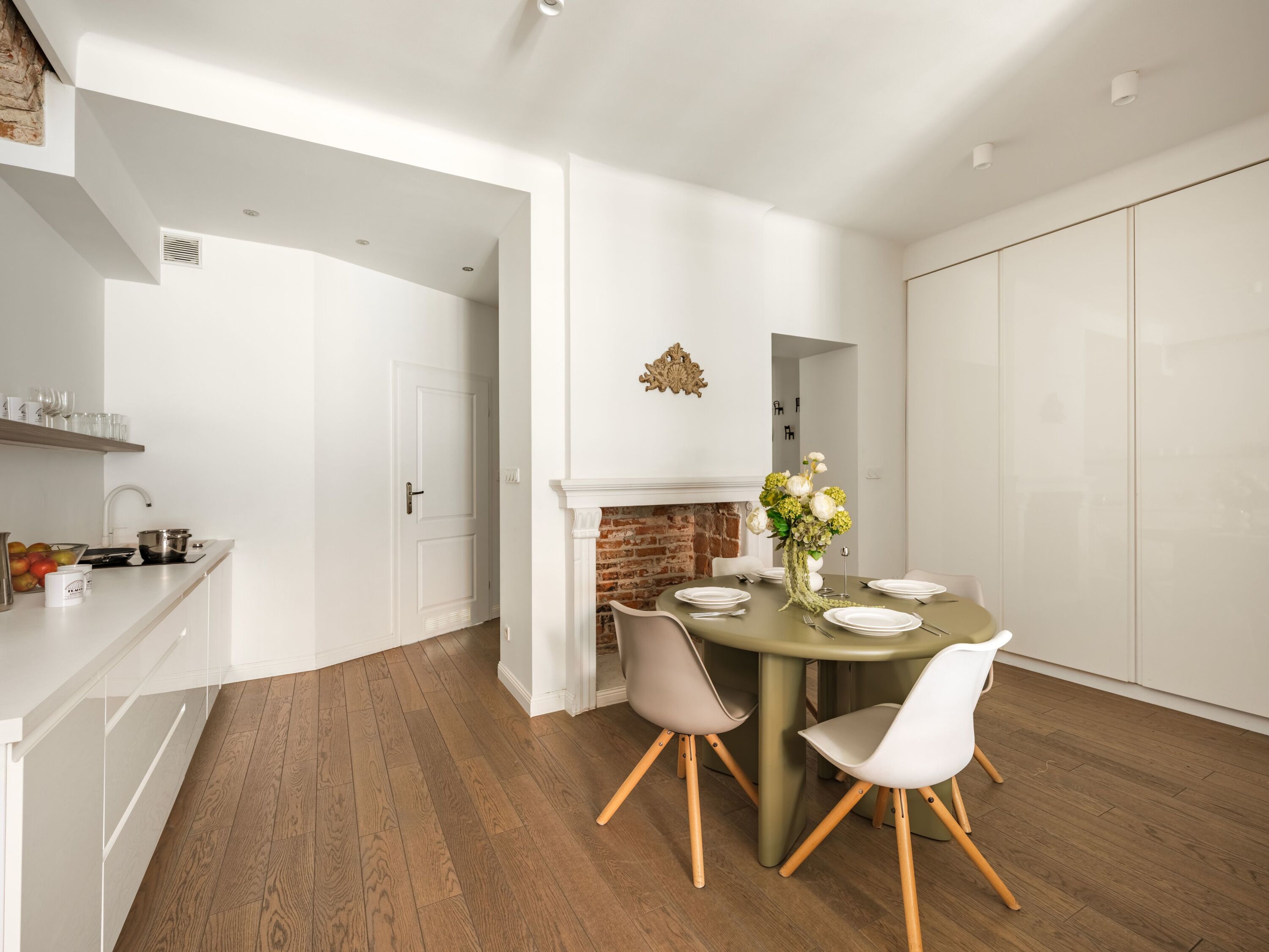 A modern dining area with a brick fireplace, white walls, and a wooden floor.