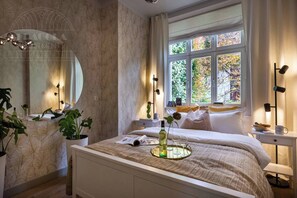 A bedroom with a bed, bedside table, window, and a mirror.