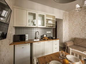 Cocina compacta con armarios blancos, microondas, pileta y comedor con mesa y sillas de madera.