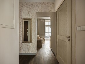 Un pasillo con suelo de madera, una puerta con interruptor de luz y vistas a un balcón con mobiliario exterior.