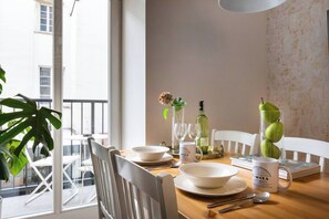 A dining area with a table set for two, featuring white plates, bowls, and a glass vase with flowers.
