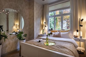 Un dormitorio con cama, mesita de noche, ventana y espejo.