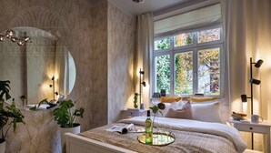 A bedroom with a bed, bedside table, window, and a mirror.