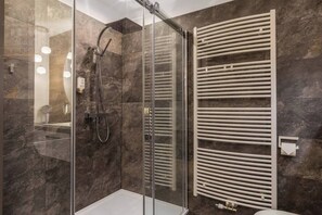 A modern bathroom with a glass shower enclosure, a white towel rack, and a marble-tiled wall.