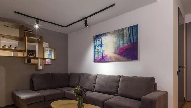 Un salon moderne avec un canapé d’angle, une table basse ronde et un tableau accroché au mur.