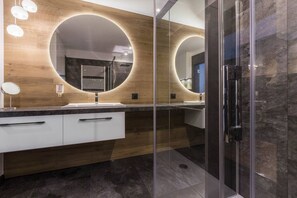 Un baño moderno con tocador de madera, dos lavamanos y cabina de ducha de vidrio.