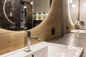 Ein modernes Badezimmer mit einem Holzkosmetikschrank, einem großen Spiegel und einem eleganten Wasserhahn.