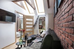 A cozy living room with a sofa, a small table, a TV, and a skylight.
