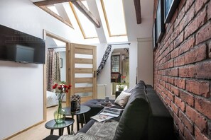 A cozy living room with a sofa, a small table, a TV, and a skylight.