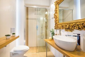 A modern bathroom with a glass shower enclosure, a white sink, and a large ornate mirror.