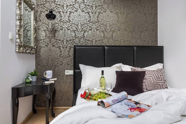 A hotel room with a bed, a bedside table with a lamp, a mirror, and a patterned wallpaper.