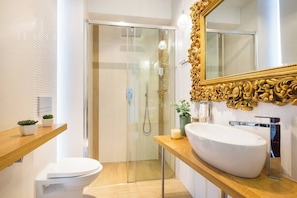A modern bathroom with a glass shower enclosure, a white sink, and a large ornate mirror.