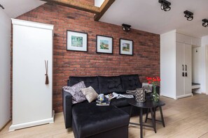 A living room with a brick wall, a black sofa, a coffee table, and a white wardrobe.