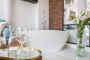 Un baño moderno con una bañera independiente, cabina de ducha con mampara de vidrio y un florero con flores sobre una mesa.