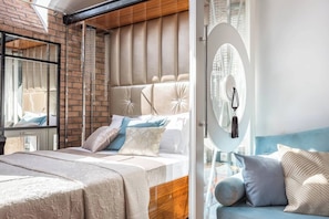 Une chambre à coucher moderne avec un mur en briques, une tête de lit capitonnée, un grand miroir et un canapé bleu.