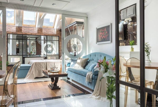 A modern living room with a blue sofa, a dining table, and a large mirror.