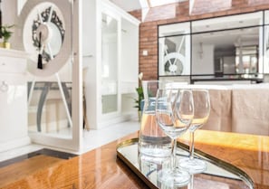 Un interior moderno con un comedor que presenta una mesa de madera con una bandeja de vidrio que contiene copas de vino y un vaso de agua.