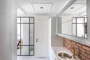A bathroom with a white vanity, a large mirror, a brick accent wall, and a modern faucet.