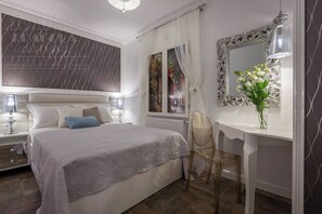 A bedroom with a bed, bedside tables, a desk, a chair, a mirror, and a window with curtains.