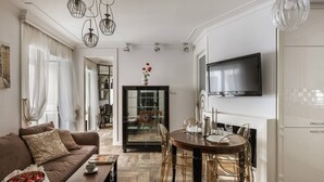 A modern living room with a sofa, dining table, and chairs, a television, and a kitchen area. - Glossy 2-bed apartment (Kraków)