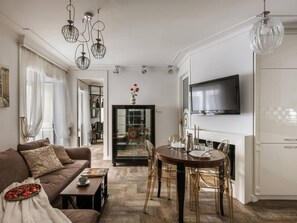 A modern living room with a sofa, dining table, and chairs, a television, and a kitchen area. - Glossy 2-bed apartment (Kraków)
