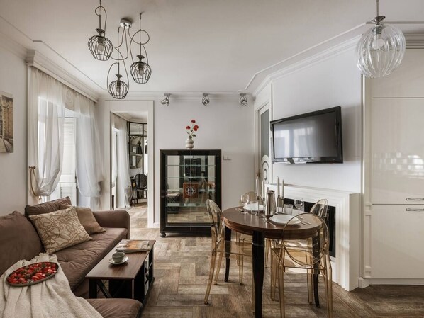 A modern living room with a sofa, dining table, and chairs, a television, and a kitchen area.