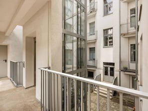 Um edifício residencial de vários andares com varandas, uma escadaria central e um corredor que leva a uma porta.