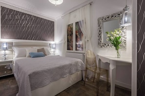 A bedroom with a bed, bedside tables, a desk, a chair, a mirror, and a window with curtains.
