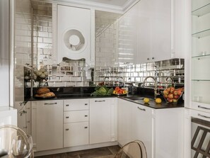 Cozinha moderna com armários brancos, bancada preta e painel de vidro.