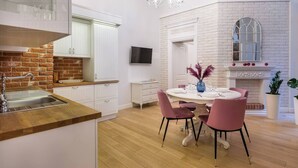 A modern kitchen with white cabinetry, a brick accent wall, a dining area with pink chairs, and a fireplace. - Magnifique 2-bed apartment (Kraków – Old Town)