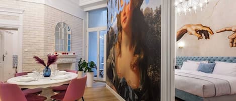 Un interior moderno con una zona de comedor, un cuadro grande y un dormitorio con cabecero tapizado.